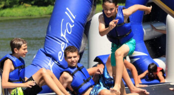 boys jumping off a lake inflatable.